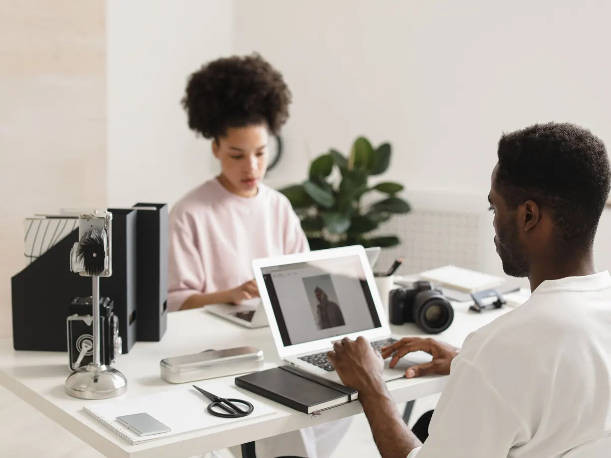 Two creative professionals collaborating with laptops in a bright workspace
